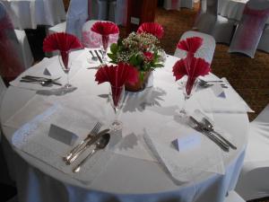 a white table with red flowers and silverware on it at Dinorben Arms Hotel in Amlwch