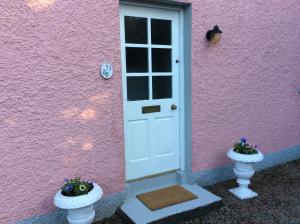 a pink house with a white door and two vases at Hallmount Cottage - Belfast in Belfast
