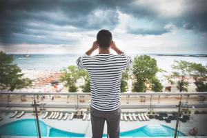 a man standing on a balcony looking at the beach at Hotel Bavaria Blu in Mamaia