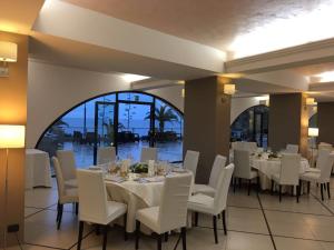 a dining room with white tables and chairs and a large window at Elihotel in SantʼAlessio Siculo