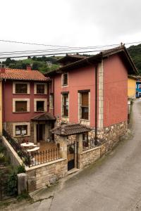 une maison rouge avec une clôture en face d'une rue dans l'établissement Apartamentos la Regoria, à Arenas de Cabrales