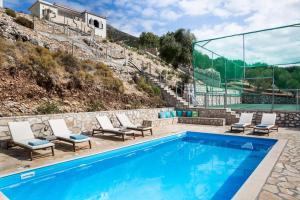 a swimming pool with chairs and a tennis court at Myrtos Bay Apartments in Anomeriá