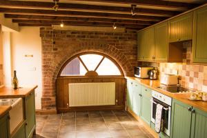 a kitchen with green cabinets and a brick wall at Lodge Barns in Fiskerton