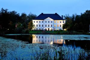 ein großes weißes Haus mit einem Teich davor in der Unterkunft Schlossgut Gross Schwansee in Groß Schwansee