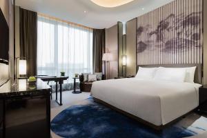 - une chambre avec un grand lit blanc et un bureau dans l'établissement Wanda Realm Hotel Wuhu, à Wuhu