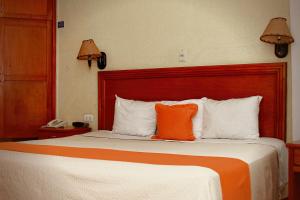 Hotel Báez Carrizal في فيلاهيرموسا: وسادة برتقال على سرير في غرفة الفندق