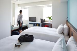 a hotel room with two beds and a person walking through the window at the b shimbashi toranomon in Tokyo