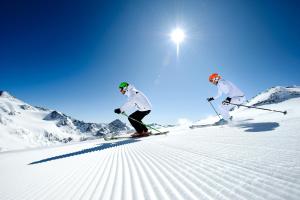 two people are skiing down a snow covered slope at Hotel Almhof in Neustift im Stubaital