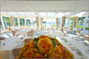 un ristorante con tavoli e sedie bianchi e una rosa gialla di Strauers Hotel am See a Bosau