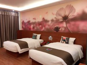 two beds in a room with a flower painting on the wall at Pai Hotel Jiuquan Jianshe Road Ouzhou Yuan in Jiuquan