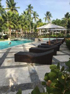 a pool with benches and an umbrella and palm trees at Apartment Balcones Del Atlantico in Las Terrenas