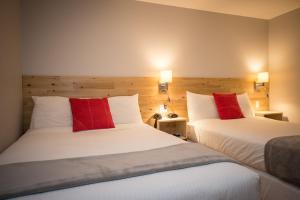 two beds with red pillows in a hotel room at Motel Colonial in Rimouski