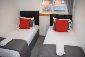 2 camas individuais num quarto com almofadas vermelhas em Kelpies Serviced Apartments- Russell em Falkirk
