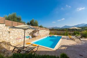 a pool with chairs and an umbrella next to a stone wall at Villa Irene & Villa Sylvia in Roumelí