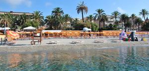 a beach with chairs and tables and palm trees and water at Albergo Villagrande in Varazze