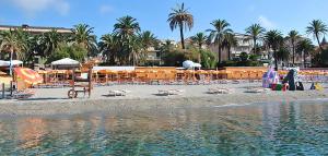 una playa con sillas, mesas, palmeras y agua en Albergo Villagrande, en Varazze