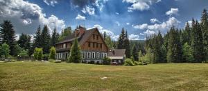 une grande maison sur un champ verdoyant avec des arbres dans l'établissement Hotel Perla Jizery, à Josefův Důl