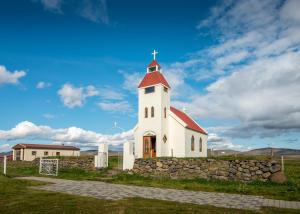 a white church with a red roof and a stone wall at Fjalladýrð Guesthouse in Modrudalur