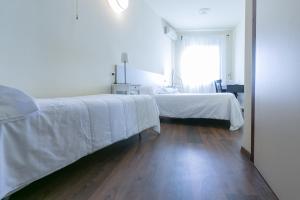 a bedroom with a bed with white sheets and a wooden floor at Albergo Il Cochino in Montale