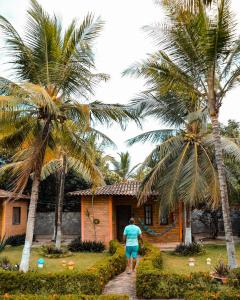 a person walking past a house with palm trees at Pousada do Riacho in Barreirinhas