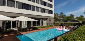 a swimming pool in front of a building with pink swans at Rydges Bankstown in Bankstown