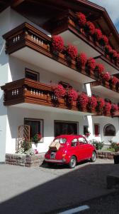 une voiture rouge garée devant un bâtiment dans l'établissement Hotel Garni Walter, à Ortisei