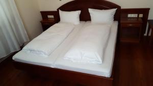 Una cama con sábanas blancas y almohadas. en Gaststätte Peperoni en Biberach an der Riß