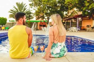 un homme et une femme assis à côté d'une piscine avec des verres à vin dans l'établissement Hotel do Grande Rio, à Petrolina