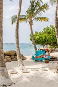 a woman sitting on a chair on the beach at Serene by the Sea in Savaneta