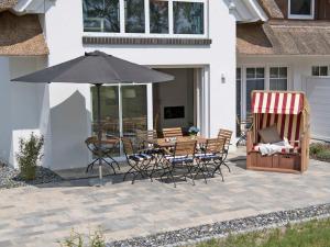 a patio with a table and chairs and an umbrella at Reetperle Lobbe - Ferienhaus mit Sauna (F 650) in Lobbe