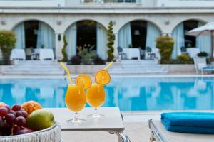 two glasses of orange juice on a table next to a pool at Rodos Park in Rhodes Town