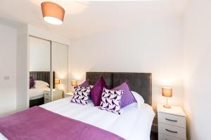 ein Schlafzimmer mit einem großen Bett mit lila Kissen in der Unterkunft Abodebed Oval View Apartments in Hemel Hempstead