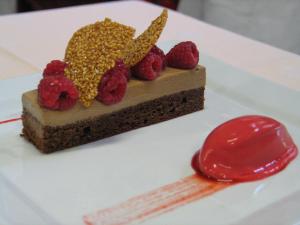 un trozo de pastel de chocolate con frambuesas en un plato en The Originals City, Hôtel de France, Bessines-sur-Gartempe (Inter-Hotel), en Bessines-sur-Gartempe