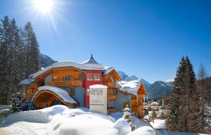 Un edificio en la nieve con el sol detrás. en Cristal Palace Hotel, en Madonna di Campiglio