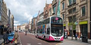 a double decker bus driving down a city street at Maldron Hotel Belfast City in Belfast +19 photos