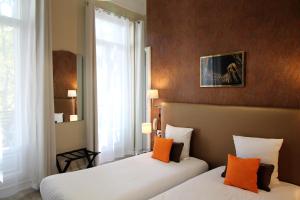 two beds in a hotel room with orange pillows at Régina Boutique Hotel in Avignon