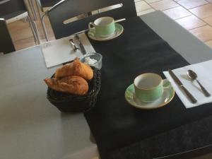 einen Tisch mit zwei Tassen und einem Korb Brot in der Unterkunft Logis Hotel Restaurant Le Flamant Rose camargue in Albaron