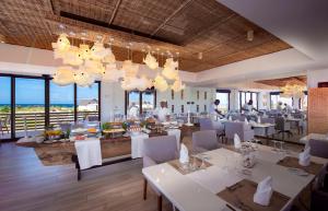 un restaurante con mesas blancas, sillas blancas y ventanas en Mequfi Beach Resort en Mecúfi