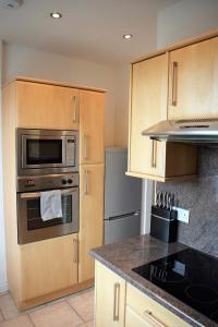 una cocina con electrodomésticos de acero inoxidable y armarios de madera en Kelpies Serviced Apartments MacGregor- 2 Bedrooms, en Grangemouth