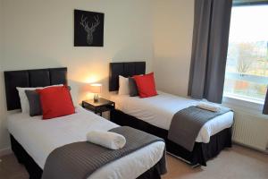 1 dormitorio con 2 camas con almohadas rojas y ventana en Kelpies Serviced Apartments MacGregor- 2 Bedrooms, en Grangemouth