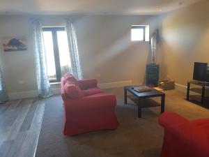 a living room with a red chair and a tv at Oak & Hazel, Heath Row Barn in Overton