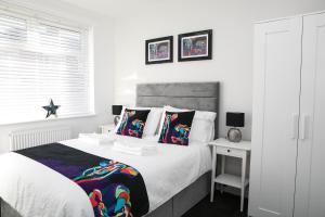 a white bedroom with a large bed with colorful pillows at Belmont Apartments in Billingham