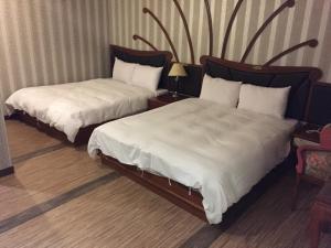 um quarto de hotel com duas camas com lençóis brancos em Bazhong Sentosa Hotel em Kaohsiung