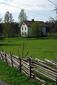 a wooden fence in front of a field with a house at Smultronboda Fårgård in Edsbruk