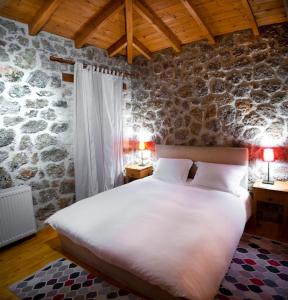 a bedroom with a large white bed in a stone wall at Levanta Guesthouse in Synikia Mesi Trikalon