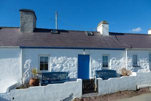 a white house with a blue door and a fence at Aberdaron Cottage 2 Bryn Chwilog in Aberdaron