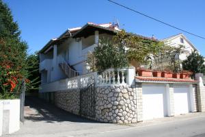 a white house with a stone fence at Apartments Galic in Rab