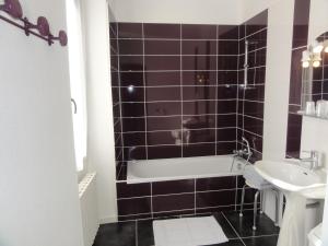 a black tiled bathroom with a tub and a sink at Hotel des Voyageurs in Payzac