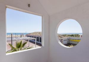 - une fenêtre ronde dans une chambre blanche avec vue sur la plage dans l'établissement Albergue Inturjoven Punta Umbría, à Punta Umbría
