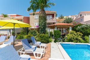 a pool with lounge chairs and an umbrella and a house at Apartments Green Harmony in Mlini